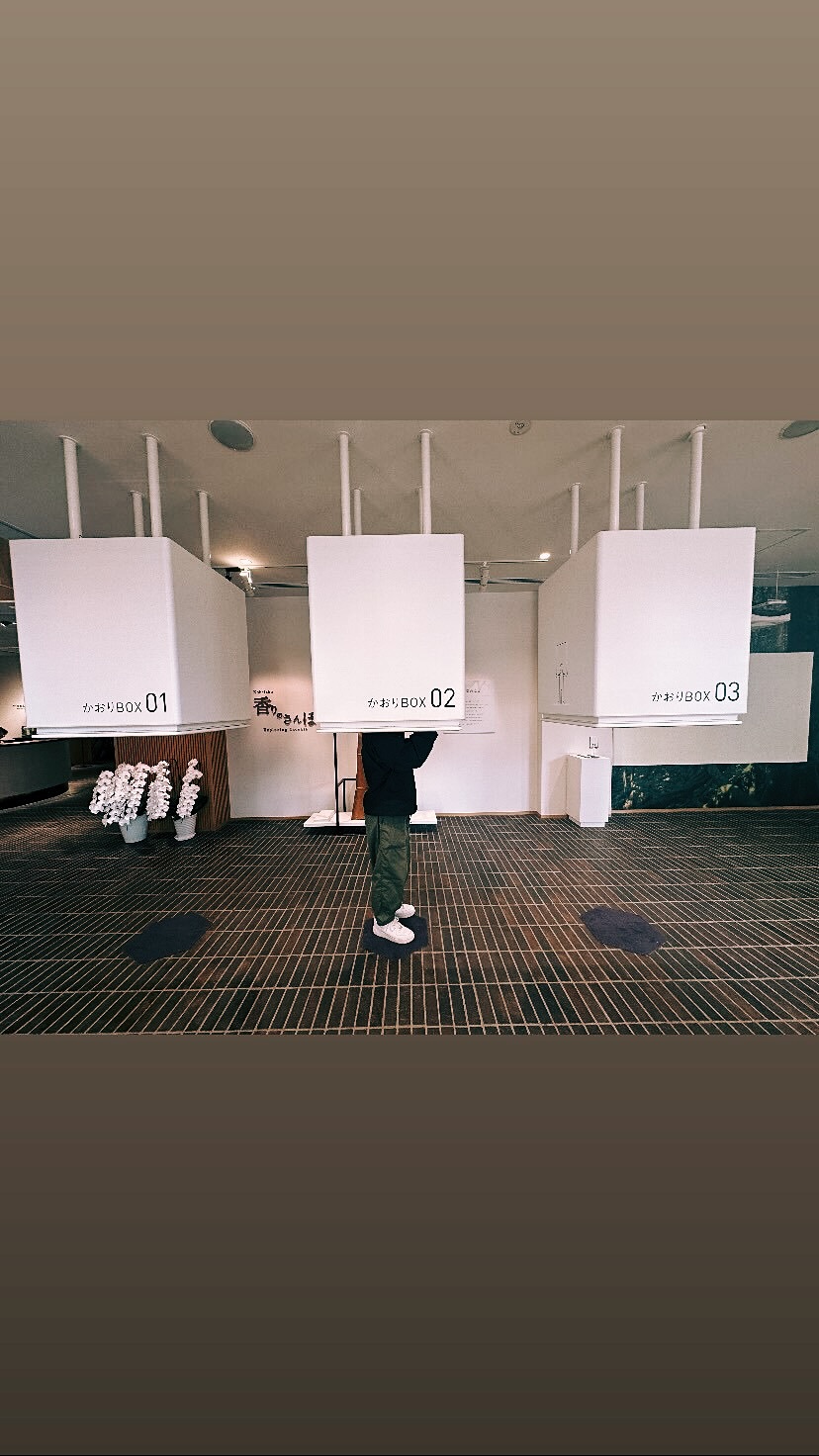 松栄堂 薫習館のかおりBOX。頭の高さに吊られた白い箱に、人が顔を近づけて香を確かめている